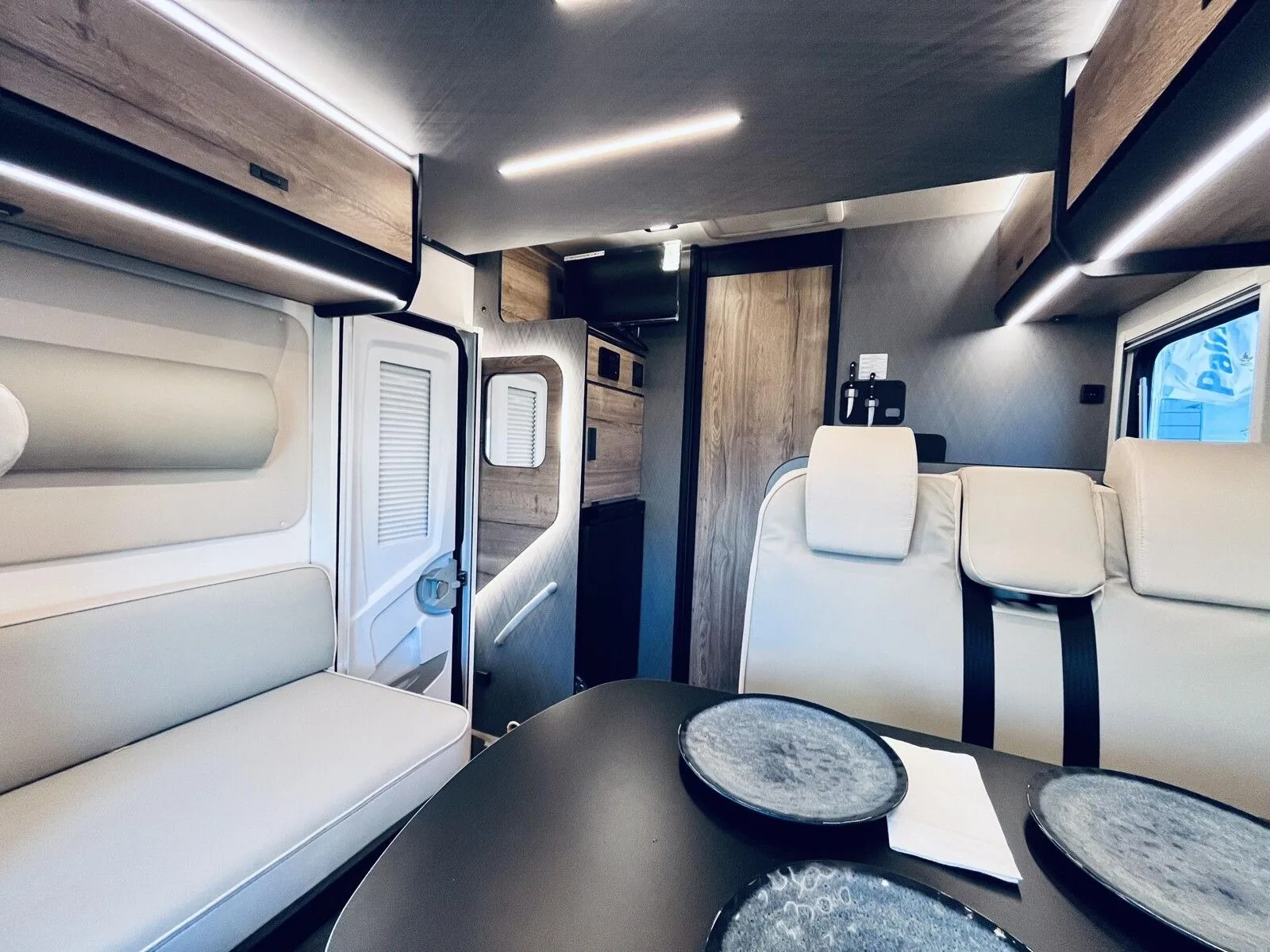 Coin salon-repas avec banquette beige, table dressée et placards hauts éclairés par des LED